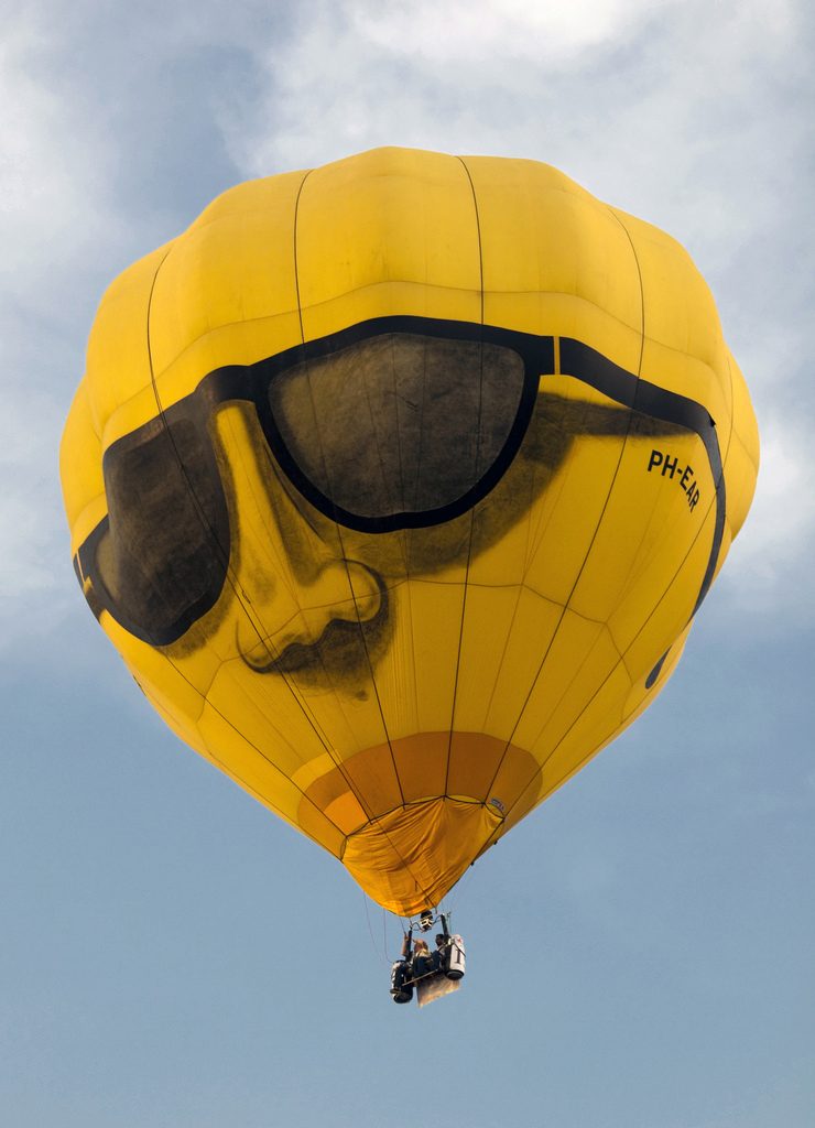 Floating high with style! A vibrant yellow hot air balloon, adorned with a cool face and sunglasses, glides across the sky.