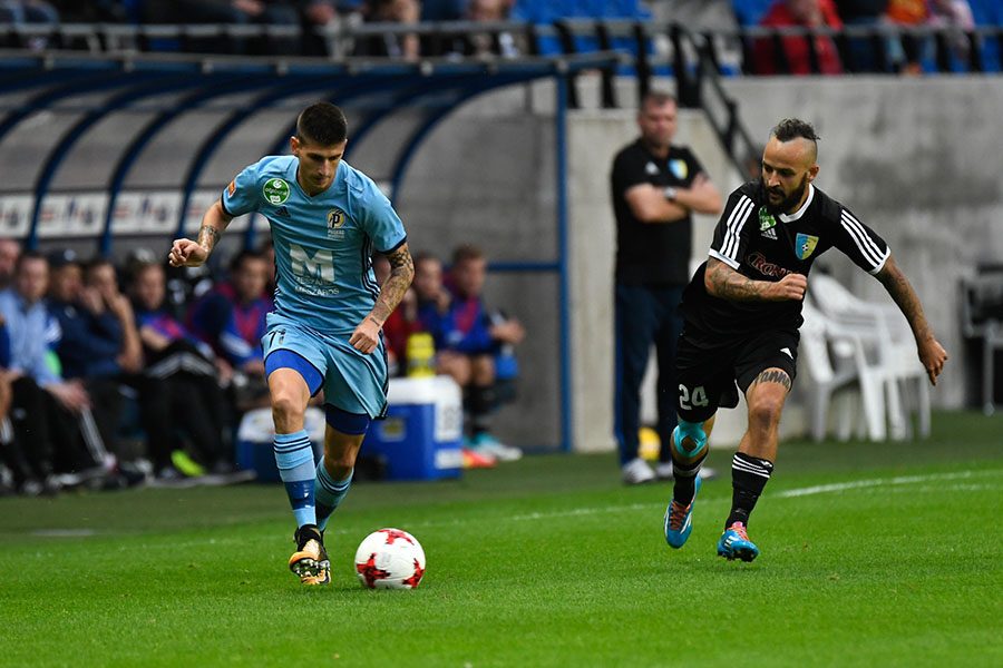 Soccer players are shown on a field and one of them is about to kick the ball.