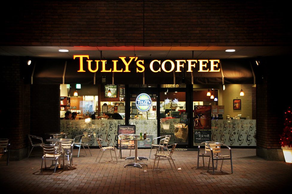 An outside view of a coffee shop. People are seen inside sitting and drinking coffee.
