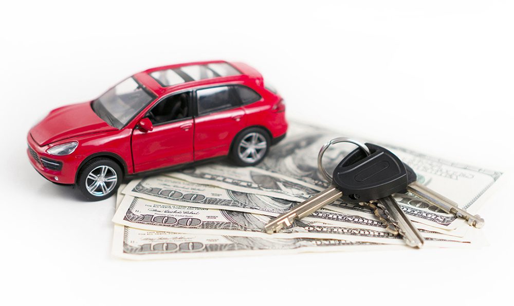 A miniature car is parked on currency notes and keys are placed next to the car.