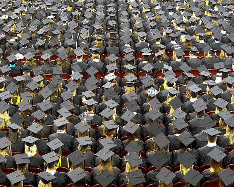 A graduate's hand is holding a rolled certificate paper tied with a ribbon.