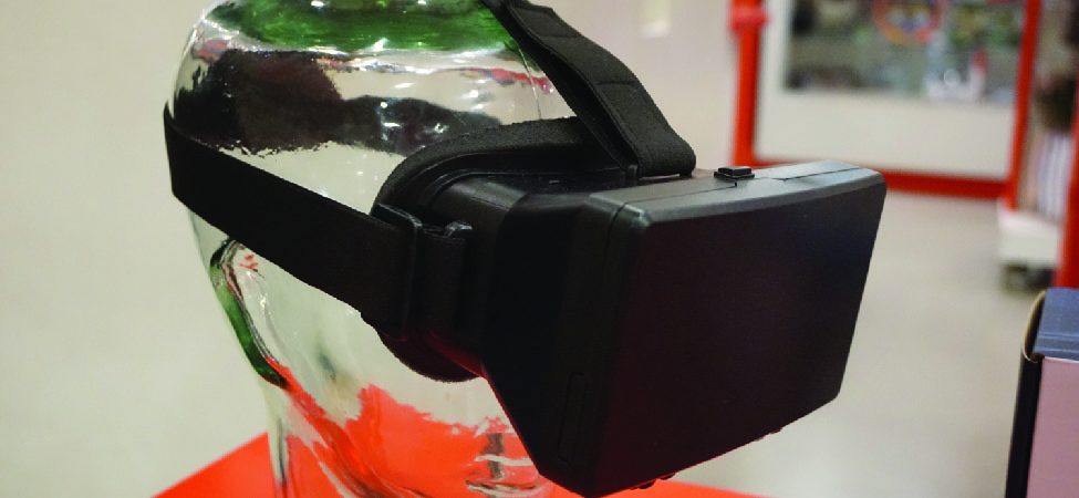 A black virtual reality headset is displayed on a clear glass head model, showcasing its design and strap details in an indoor setting with a blurred background.