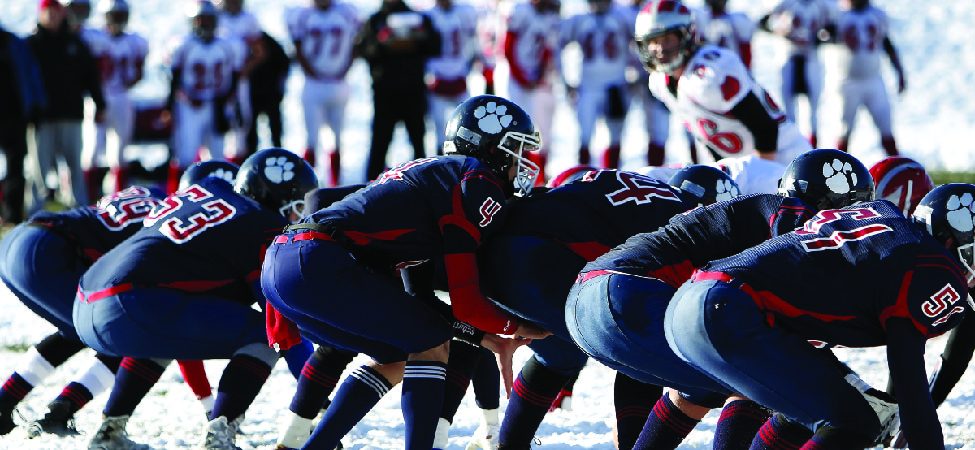 A photo of American football players lining up on the line of scrimmage.