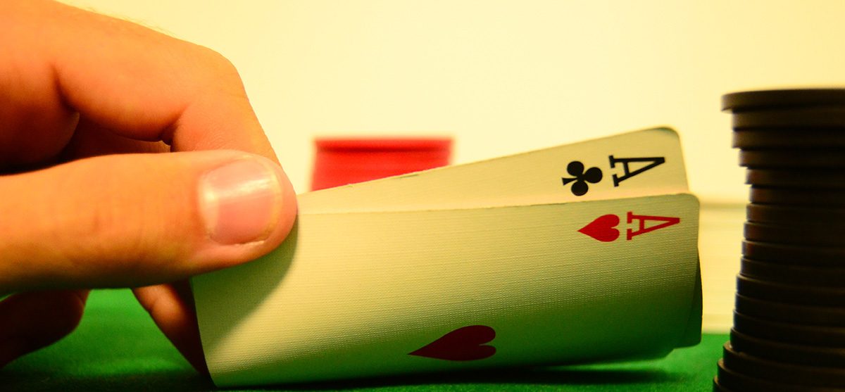 Close up of a hand lifting two playing cards at a poker table.