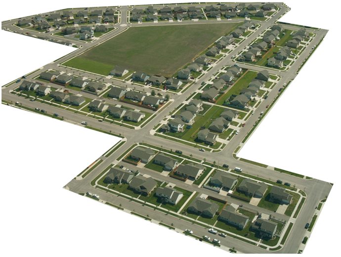 Aerial photograph of a suburban housing development: rows of single-family houses lining straight and gently curving streets around a large empty green field, the streets meeting at intersections and closing into several loops.