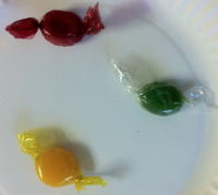 Photograph of three wrapped hard candies on a white plate — one red, one green, one yellow — the three pieces whose six possible pick-up orders the section enumerates.