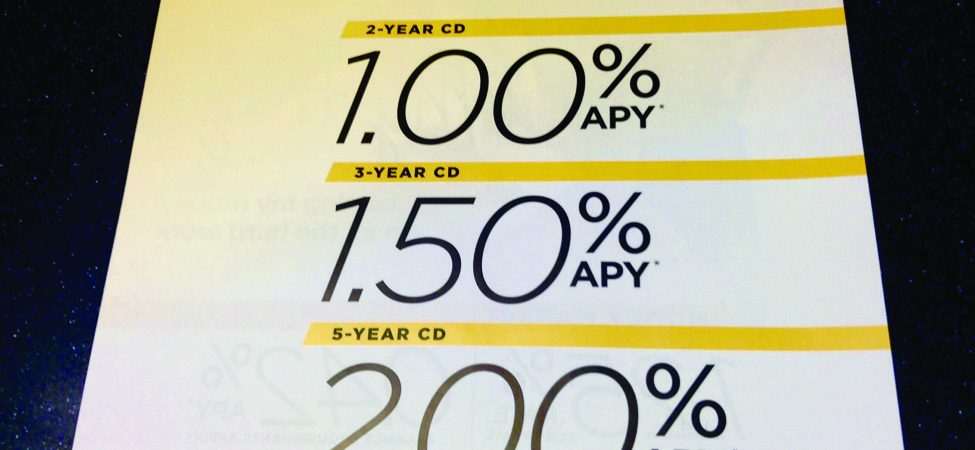 This image shows a sign at a bank indicating annual percentage rates for CDs. The top line says “Earn big with a locked-in rate”. The second line reads 2-year CD with one percent annual percentage rate; the third line reads 3-year CD with a 1.5 percent annual percentage rate, and the fourth line reads 5-year CD with a 2 percent annual percentage rate.